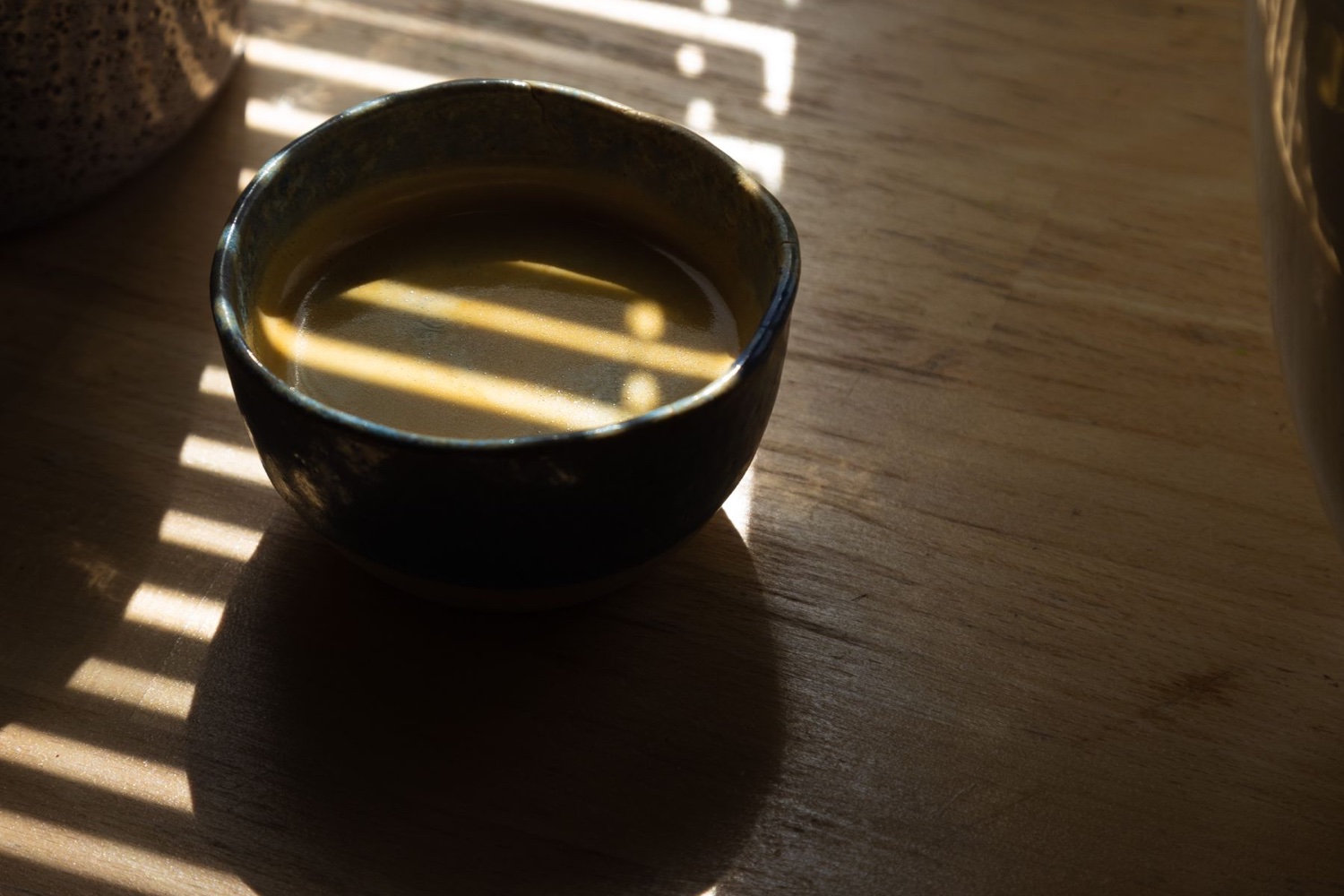 A dark ceramic coffee cup in warm window light with shadows from blinds