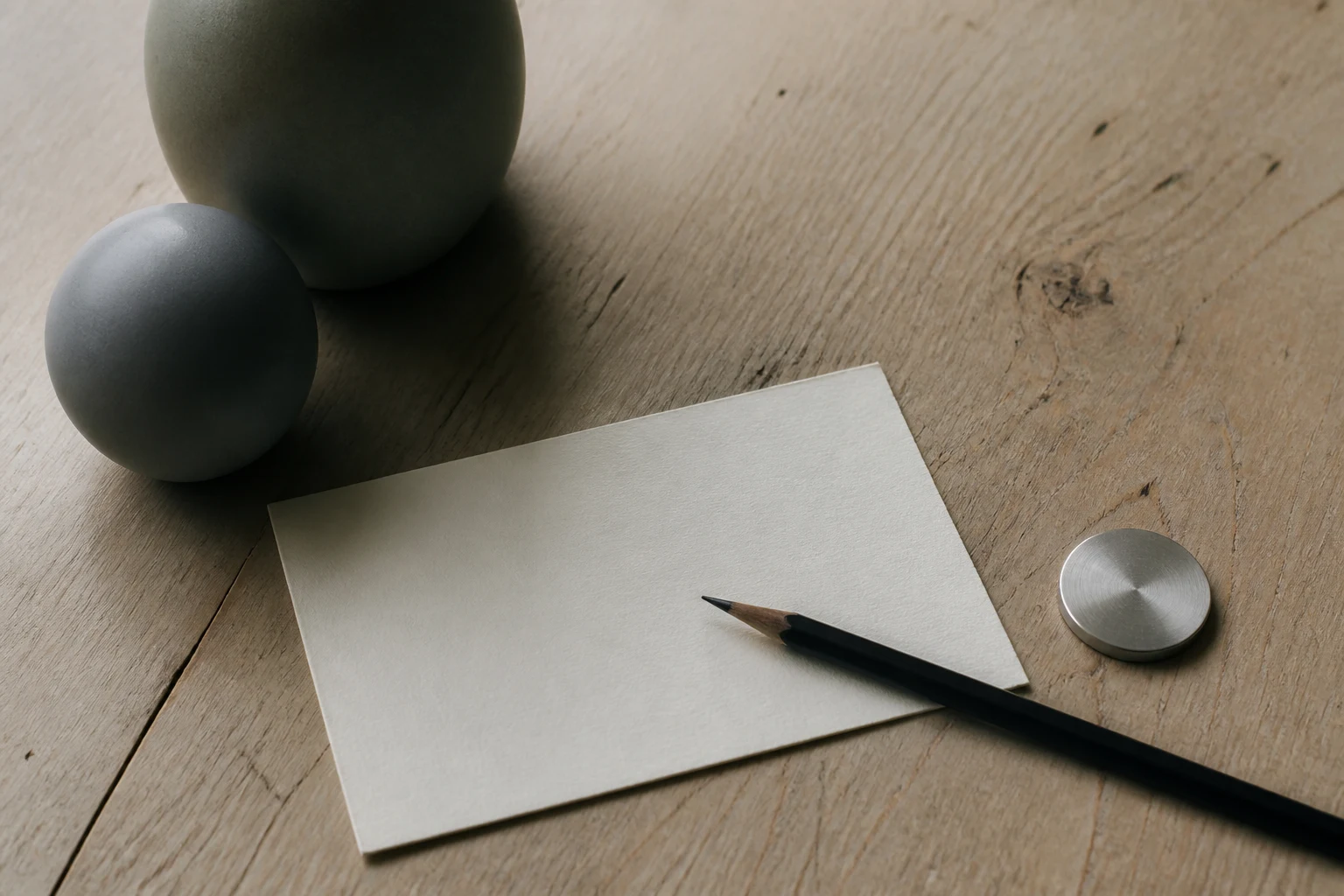 A blank consultation card, pencil and balanced ceramic forms on oak